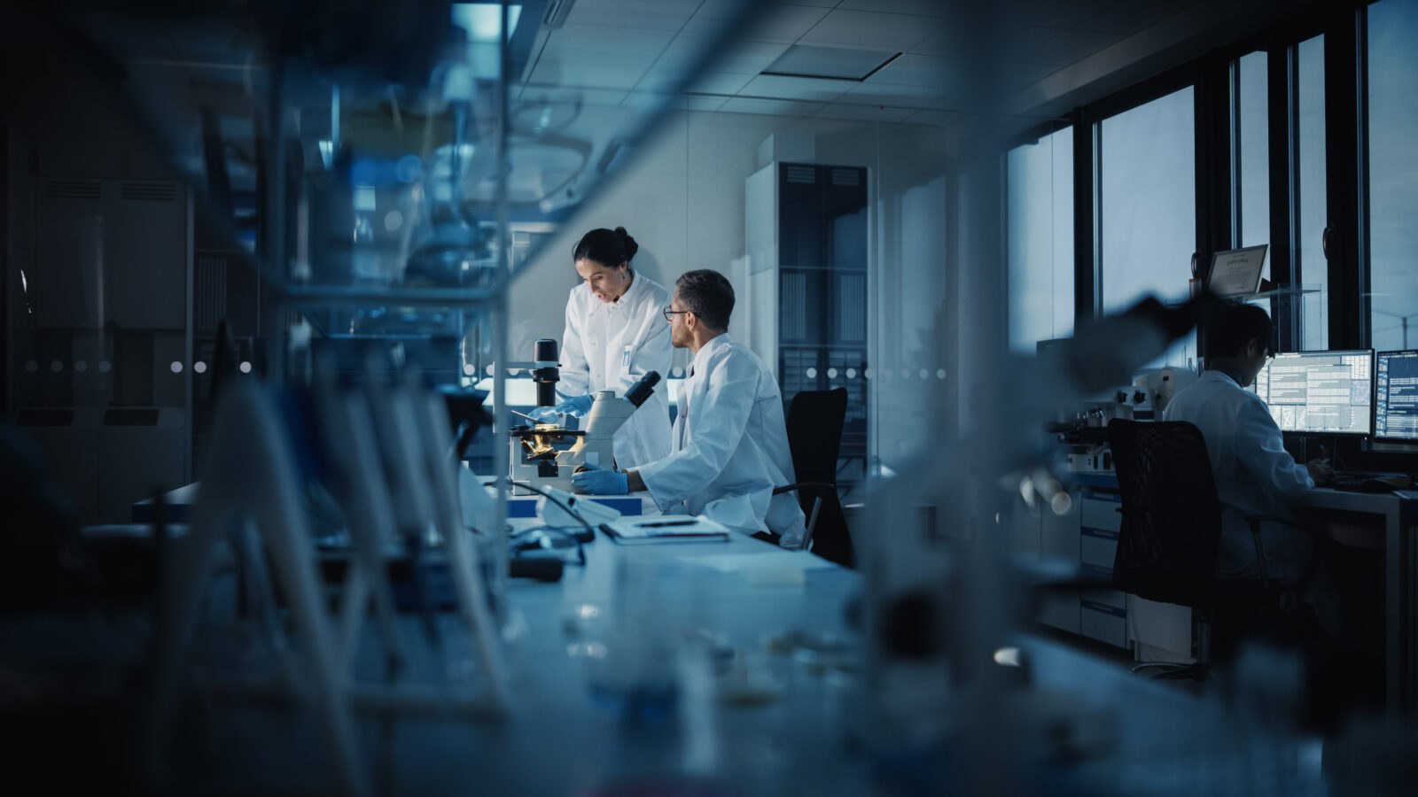 Two laboratory technicians talking highlighted by light in a dark lab