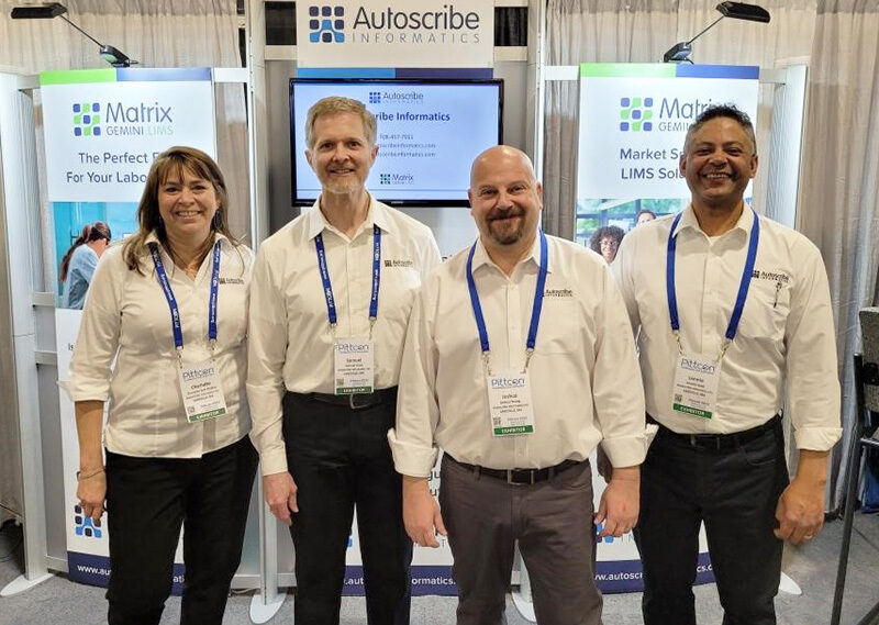 Autoscribe/Xybion staff standing on their booth at PITTCON 2023.